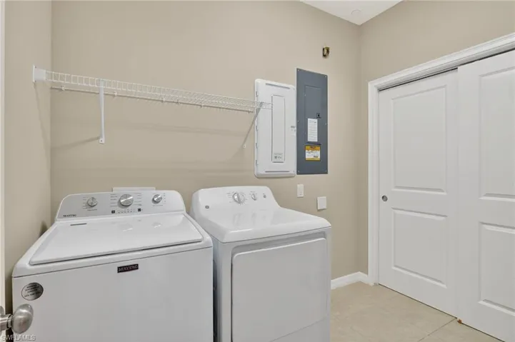 Laundry room with washing machine and clothes dryer, electric panel, and light tile patterned floors