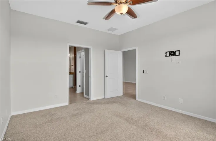 Unfurnished bedroom featuring light carpet, ensuite bathroom, and ceiling fan