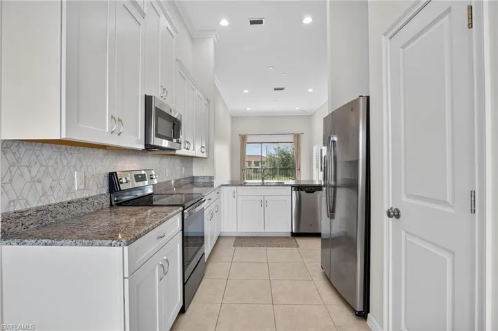 Kitchen featuring appliances with stainless steel finishes, white cabinets, light tile patterned floors, tasteful backsplash, and dark stone counters