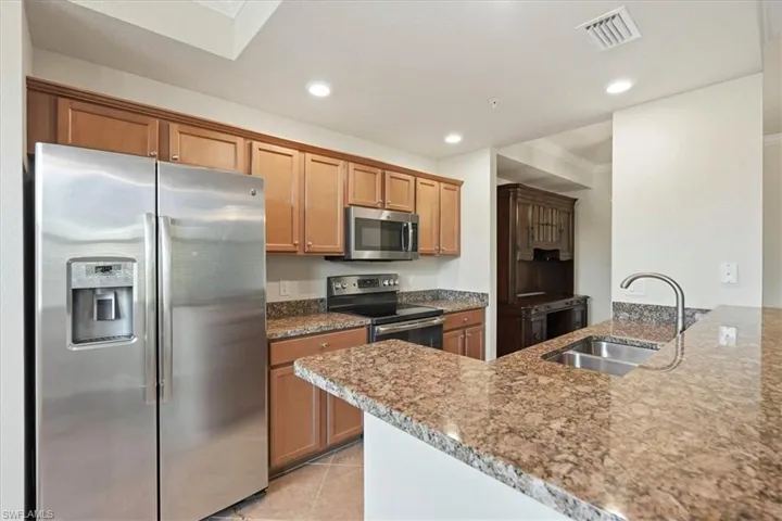 Kitchen featuring stone-patterned countertops, wooden cabinetry, stainless steel appliances, a double-basin undermount sink, and recessed ceiling lighting