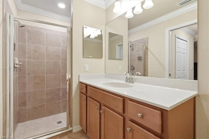 Bathroom featuring a wood-finish vanity with a white countertop, an integrated oval basin, a full-width wall mirror, and a walk-in shower with tile surround and chrome fixtures