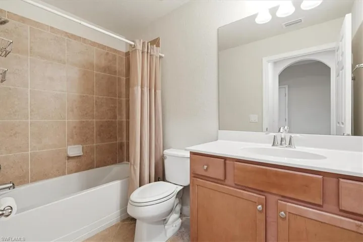 Bathroom featuring a wood-finish vanity with a white countertop, an integrated oval basin, a full-width wall mirror, and a tub-shower combination with tiled surround