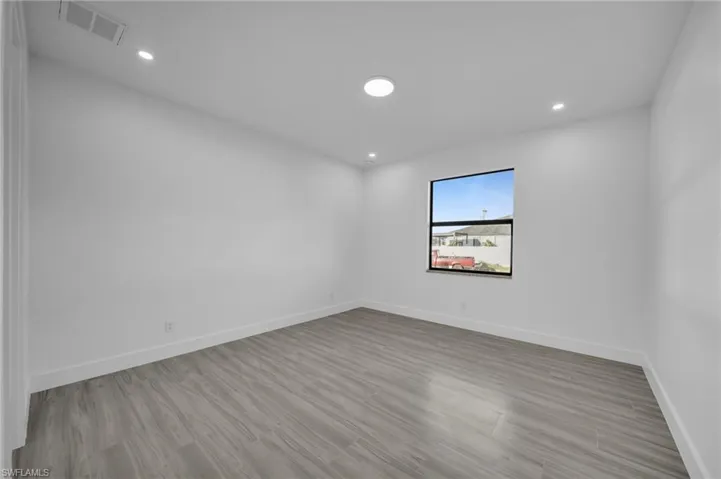 Recessed lighting, wood-finish flooring, white walls, and a black-framed window