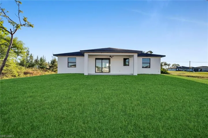 Rear exterior with a covered patio, ceiling fan, sliding glass door, and multiple windows