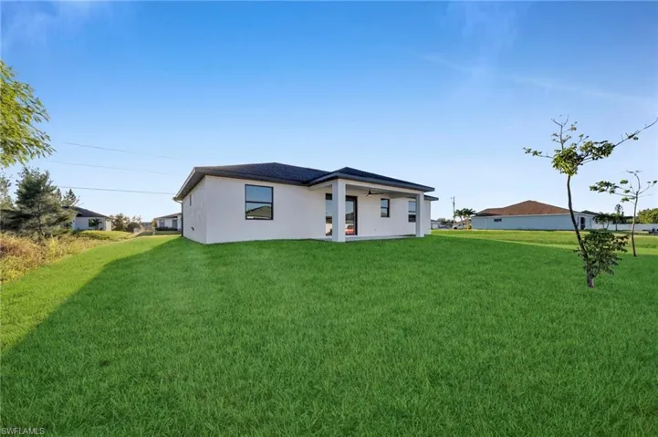 Expansive grass lawn with a stucco exterior home featuring a dark roof and covered patio