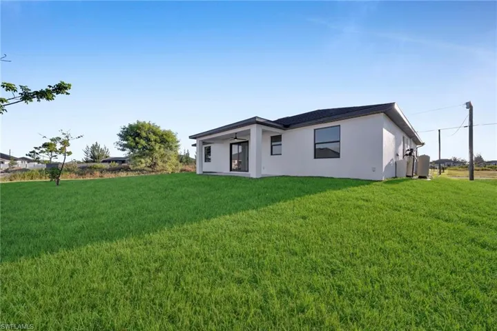 Expansive grassy yard with a covered patio, multiple windows, and a dark shingle roof
