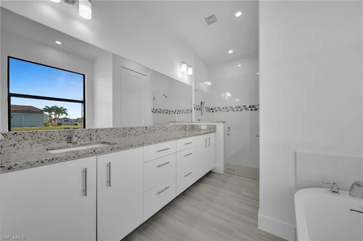 Double vanity with stone countertop, white cabinetry, undermount sinks, tile flooring, and glass-enclosed shower