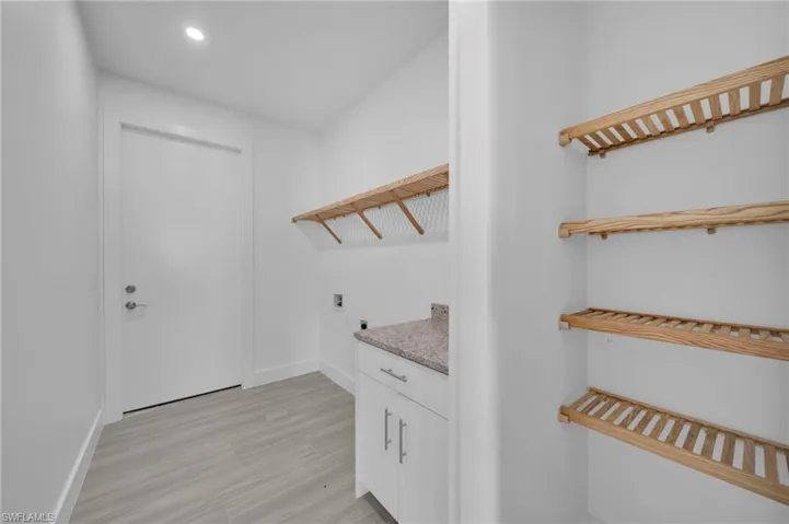 Laundry area featuring wood-finish shelving, white cabinetry, a light-colored countertop, and light-toned tile flooring