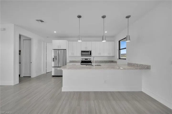 Contemporary kitchen featuring white cabinetry, stainless steel appliances, a breakfast bar, and pendant lighting