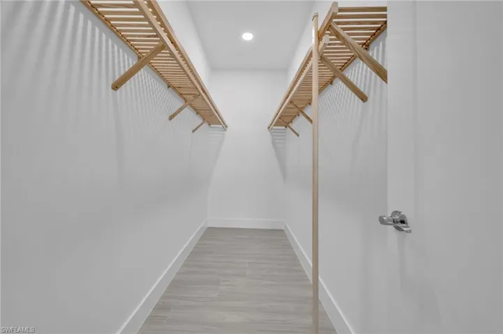 Walk-in closet with light wood shelving, white walls, and wood-finish flooring