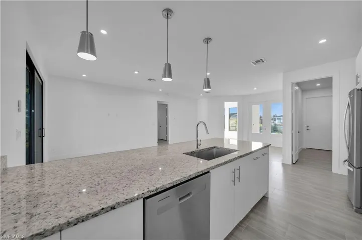 Kitchen island with a stainless steel sink and integrated dishwasher, pendant lighting, recessed ceiling lights, white cabinetry, and light-toned flooring