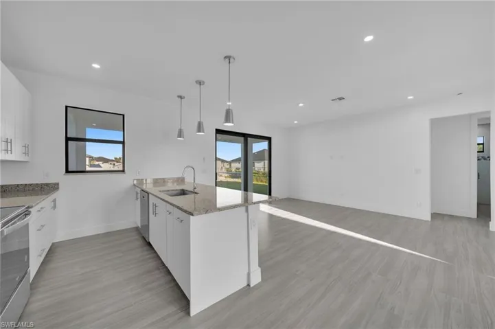 Open-concept living space with wood-finish flooring, recessed lighting, and a kitchen island featuring a stainless steel sink and pendant lighting