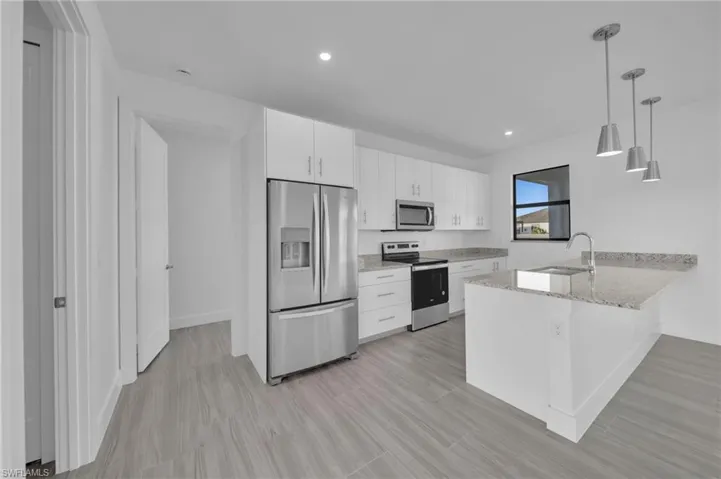 Modern kitchen featuring white cabinetry, stainless steel appliances, light-toned countertops, a kitchen island with an undermount sink, and wood-finish flooring