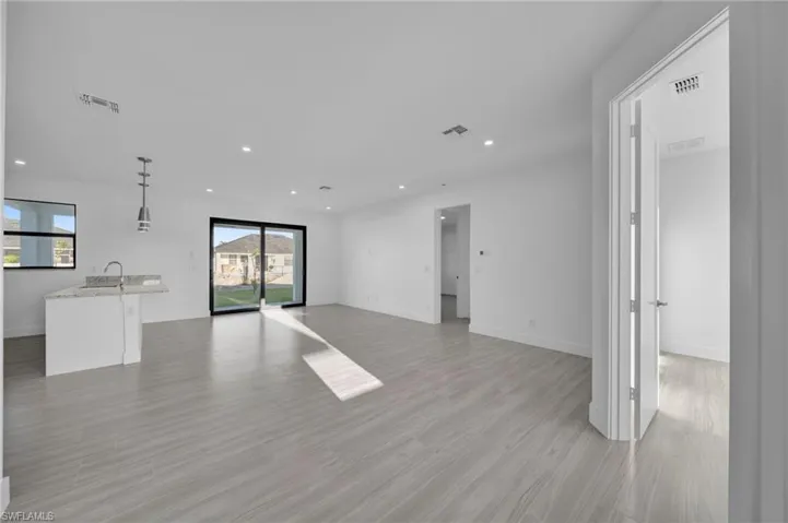 Open-concept living area featuring light-toned tile flooring, recessed lighting, and a kitchen island with a sink and pendant lighting