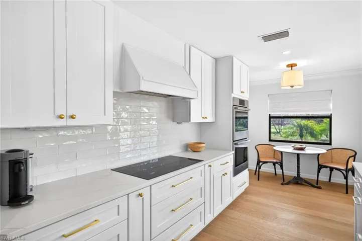 Kitchen featuring white cabinets, black electric stovetop, light wood finished floors, light stone countertops, and ornamental molding