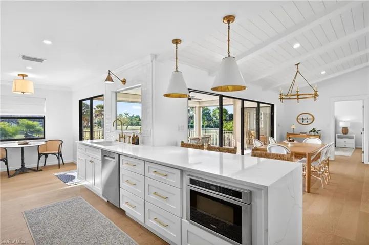 Kitchen with pendant lighting, white cabinetry, light wood finished floors, light stone counters, and lofted ceiling with beams