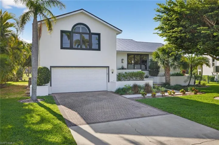 Tri-level home featuring a front yard, decorative driveway, an attached garage, stucco siding, and a metal roof