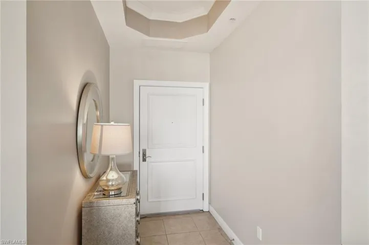 Hallway with a tray ceiling, baseboards, crown molding, and light tile patterned floors