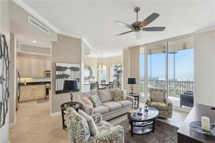 Living area featuring light tile patterned flooring, visible vents, plenty of natural light, ornamental molding, and ceiling fan with notable chandelier