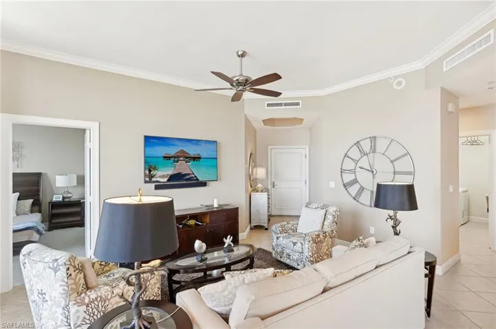 Living room featuring light tile patterned floors, ceiling fan, visible vents, and crown molding