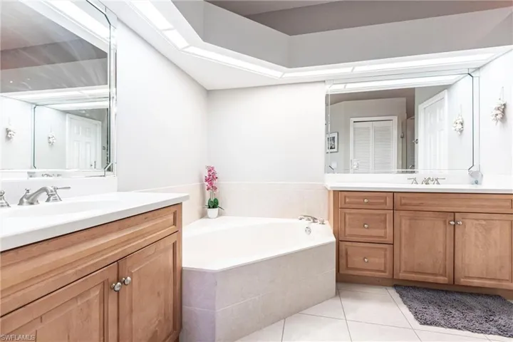 Bathroom with light tile patterned flooring, two vanities, and a bath