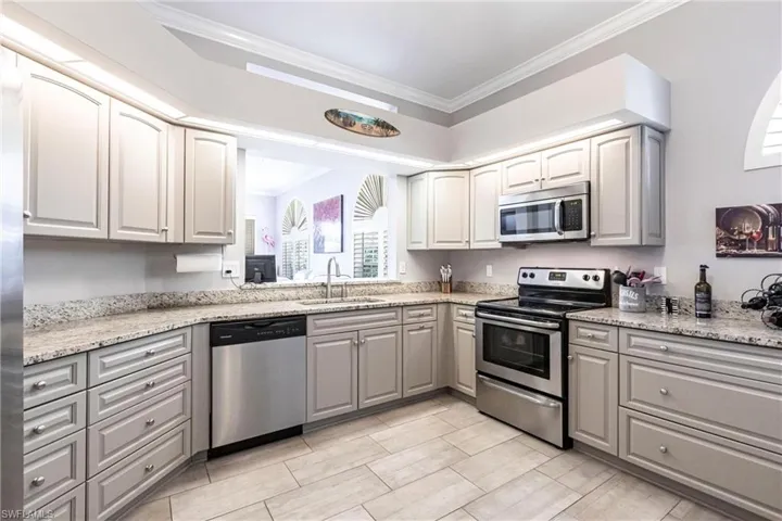 Kitchen featuring gray cabinetry, appliances with stainless steel finishes, crown molding, and light stone countertops