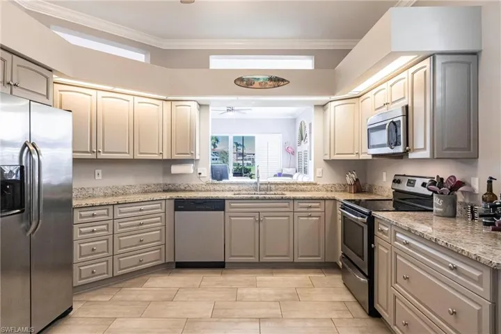 Kitchen with stainless steel appliances, crown molding, light stone counters, gray cabinets, and a ceiling fan