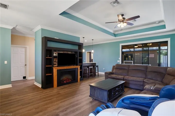 Living area featuring ornamental molding, a tray ceiling, Lifeproof LVP flooring and built-in entertainment center with fireplace.