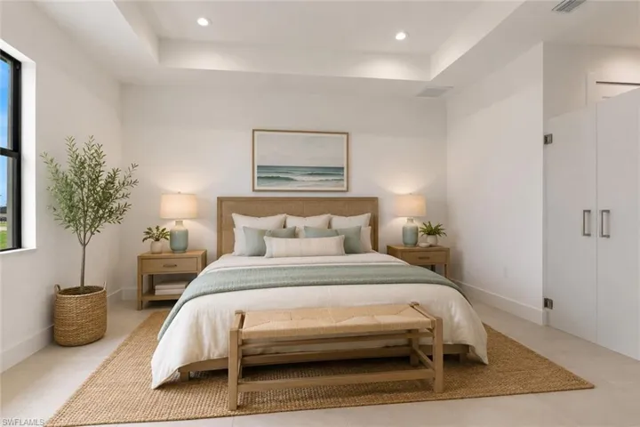 Spacious bedroom featuring light-toned flooring, a tray ceiling with recessed lighting, and a large window