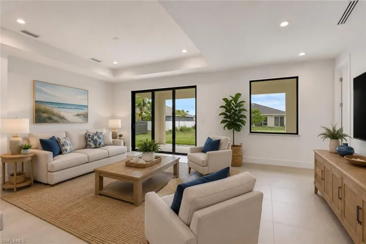 Spacious living area featuring light-colored tile flooring and tray ceilings with recessed lighting