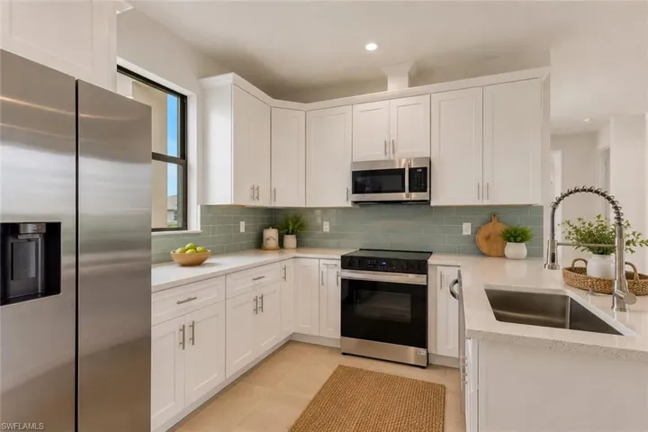 Contemporary kitchen featuring white cabinetry, light-toned countertops, stainless steel appliances, a green subway tile backsplash, and a stainless steel sink with a gooseneck faucet