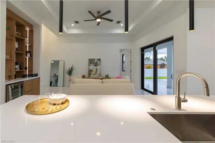 Kitchen featuring ceiling fan, beverage cooler, a tray ceiling, and sink
