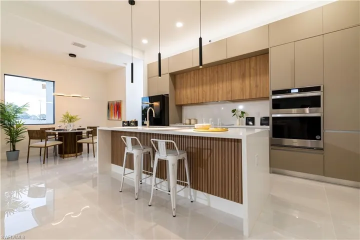 Kitchen with black fridge, stainless steel double oven, a kitchen bar, a center island with sink, and decorative light fixtures