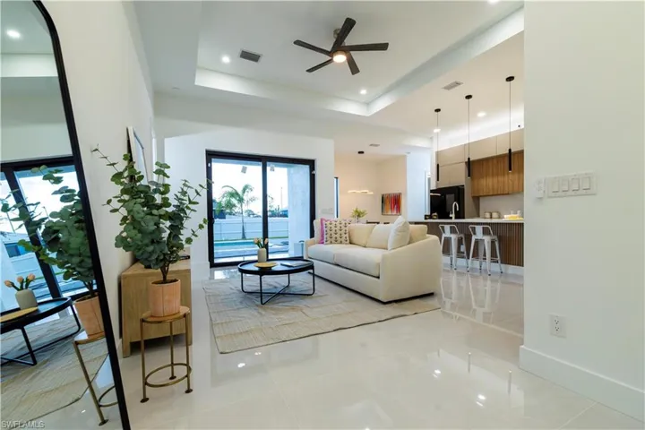 Living room with a tray ceiling, ceiling fan, and light tile patterned floors