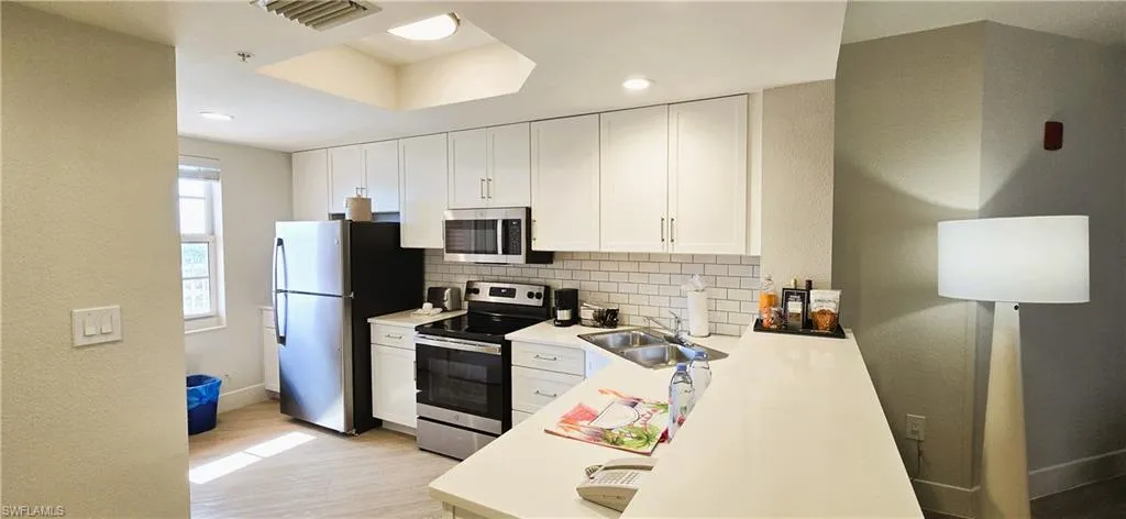 Kitchen featuring white cabinets, sink, light hardwood / wood-style floors, appliances with stainless steel finishes, and backsplash