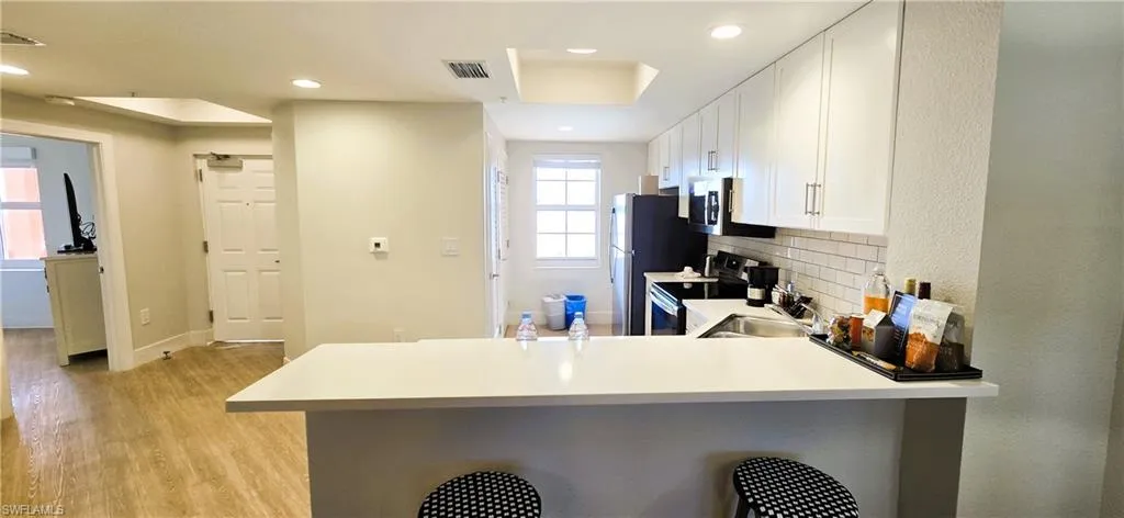 Kitchen featuring white cabinets, decorative backsplash, light wood-type flooring, appliances with stainless steel finishes, and kitchen peninsula