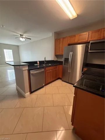 Kitchen featuring brown cabinets, refrigerator, dark stone counters, dishwashing machine, and a ceiling fan