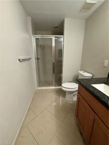 Bathroom with a textured wall, a textured ceiling, vanity, and a shower stall