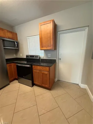 Kitchen with stove, brown cabinetry, refrigerator, dark stone counters, and a textured ceiling