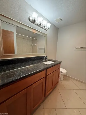 Full bathroom featuring vanity, a textured wall, light tile patterned flooring, a textured ceiling, and a shower