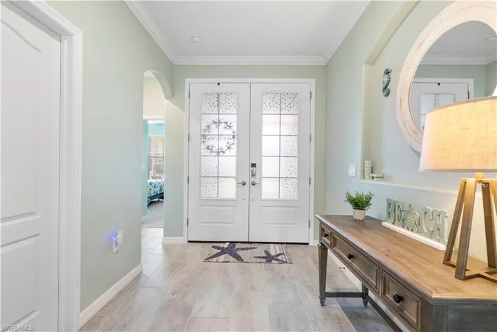 Foyer entrance featuring crown molding, french doors, arched walkways, and light wood-style floors