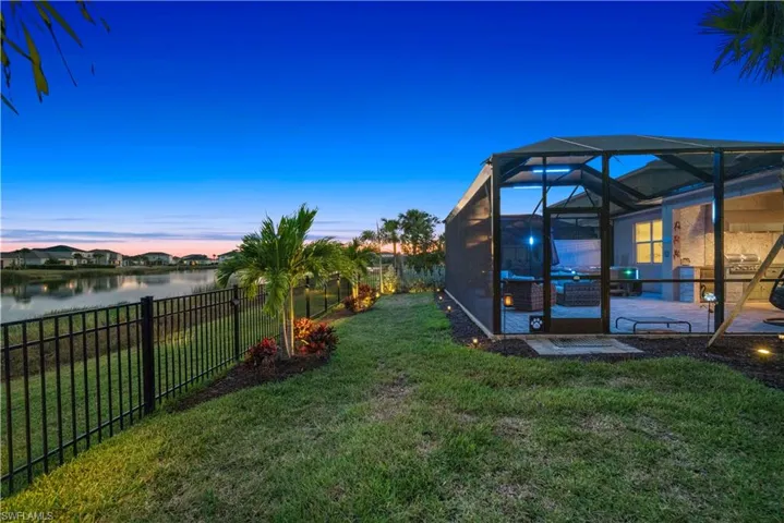Yard at dusk featuring a sunroom, a fenced backyard, glass enclosure, and a water view