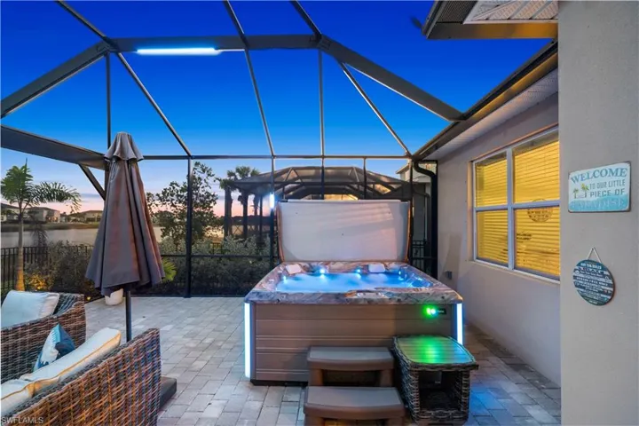 Patio terrace at dusk with a hot tub, a sunroom, glass enclosure, and a patio area
