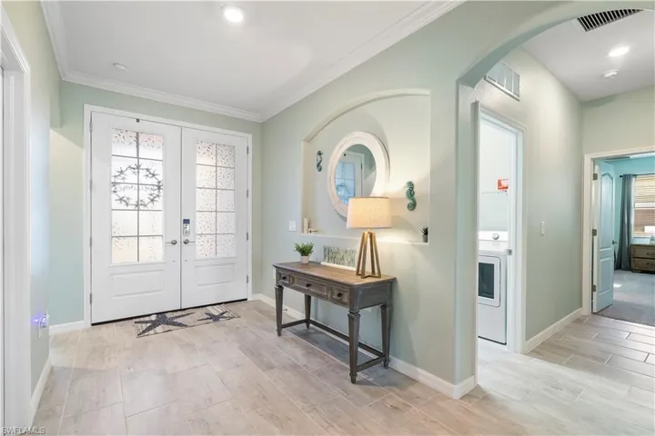 Foyer entrance featuring french doors, washer / dryer, ornamental molding, wood finish floors, and healthy amount of natural light