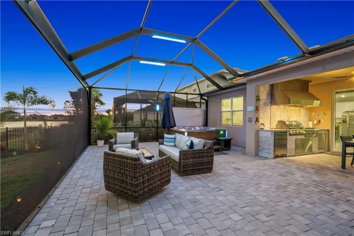 Patio terrace at dusk featuring an outdoor kitchen with living area, glass enclosure, a sunroom, and a patio area