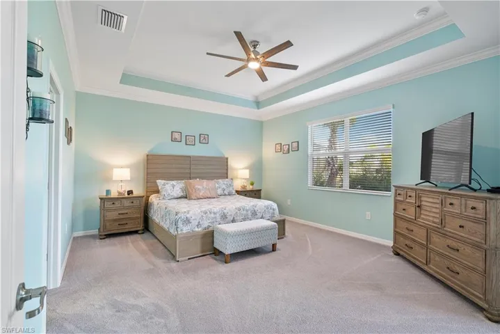 Bedroom with ornamental molding, a raised ceiling, a ceiling fan, and light colored carpet