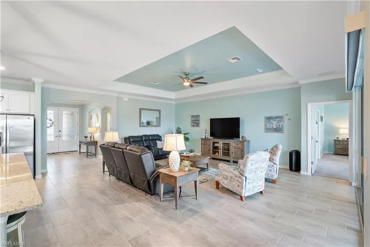 Living area with arched walkways, a raised ceiling, ornamental molding, ceiling fan, and french doors