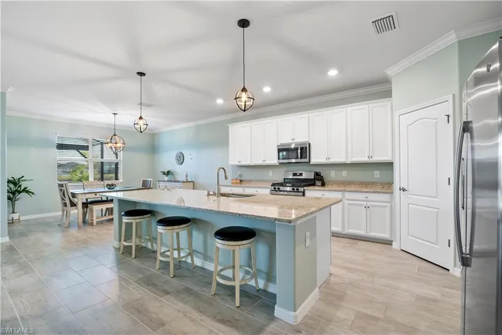 Kitchen with a kitchen breakfast bar, ornamental molding, white cabinetry, a kitchen island with sink, and decorative light fixtures