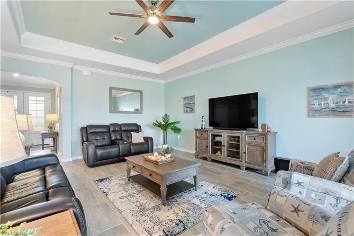 Living room featuring arched walkways, ceiling fan, a tray ceiling, ornamental molding, and wood tiled floors