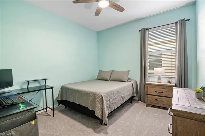 Bedroom with light colored carpet, ceiling fan, and a desk